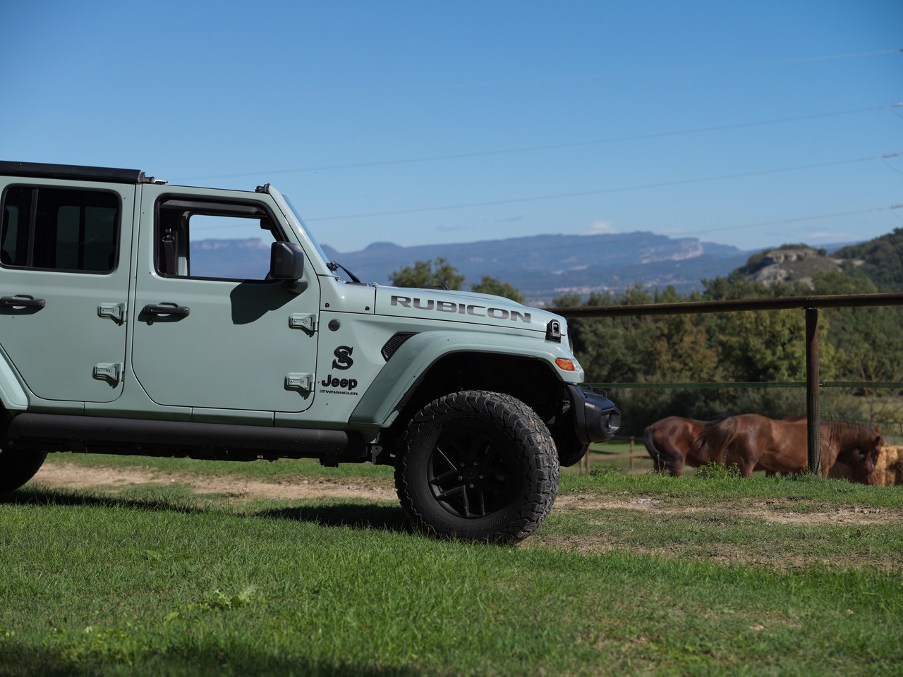 Un Jeep Wrangler Rubicon verde claro, de lado, con las montañas al fondo